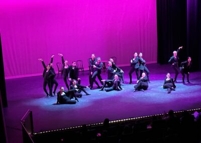 dance group in black blazers pose in blue spotlights with a pink background