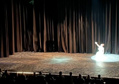 dancer in a white dress kneels in the spotlight