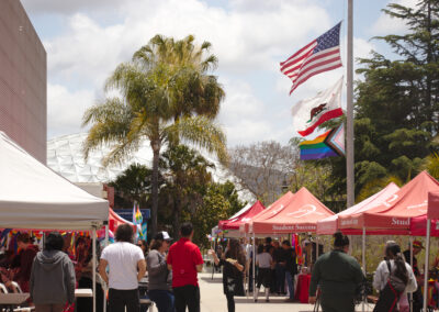row of red Palomar tents lined in front of the Dome and a flagpole with US, California, and Pride flags raised