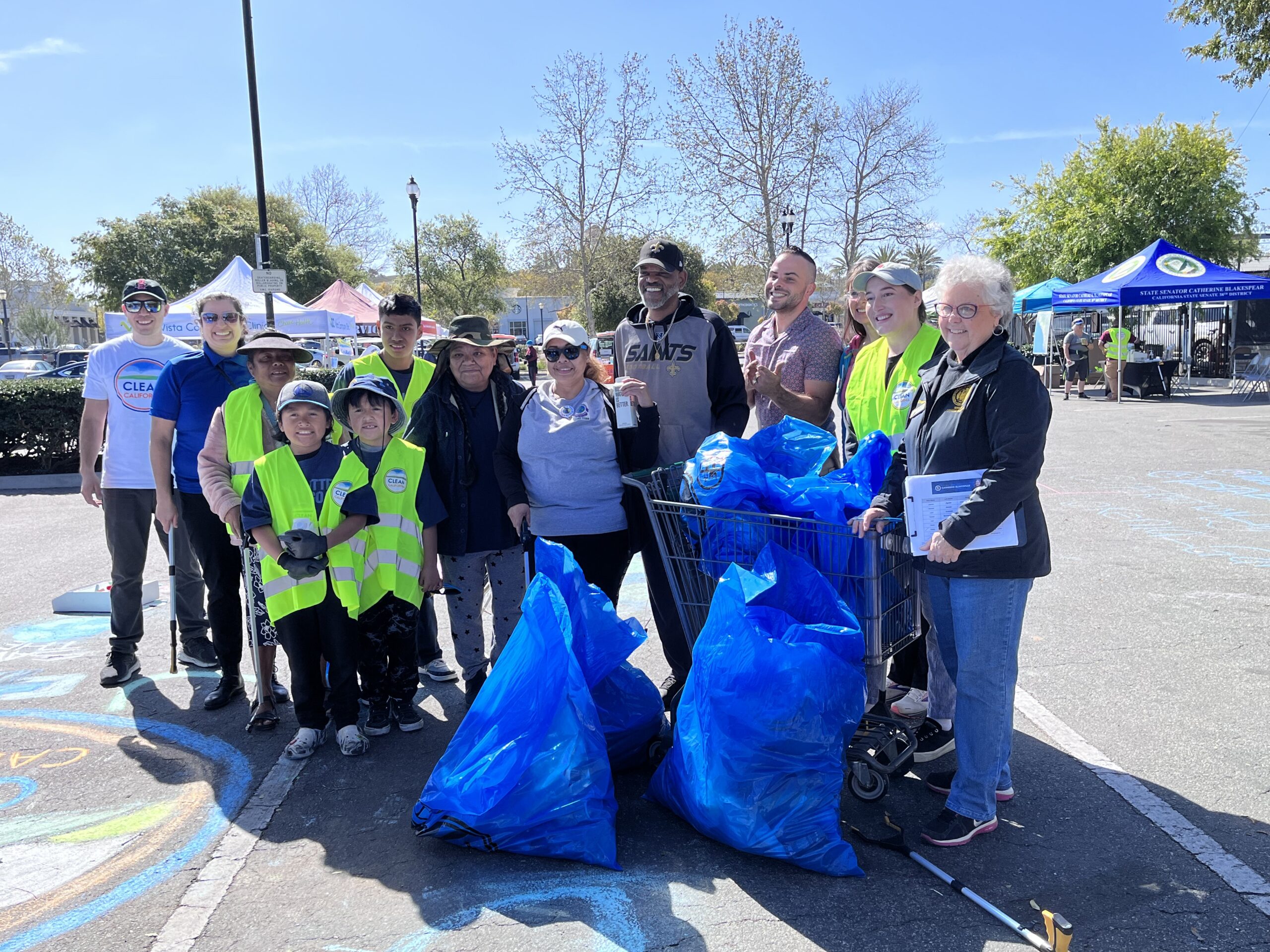 A group of people pose for a picture with several large blue trash bags with some in a shopping cart.