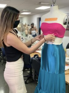 Alexis Solorio adjusts her dress design for the 2022 MODA Fashion Show. The dress top is bright pink and the dress bottom is bright blue.