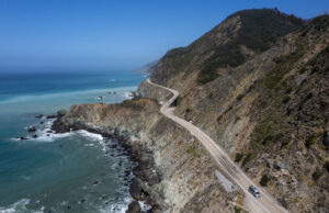 A road winds over a cliff that is above an ocean. The sky is blue that almost matches the ocean.