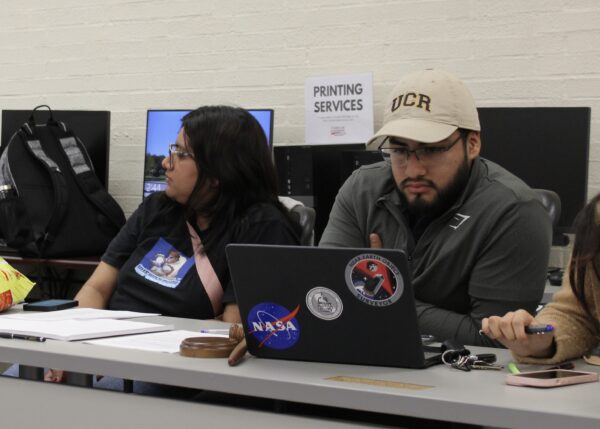 ASG President Christopher Garcia-Mendez seen reading from his laptop next to Vice President Dana Garcia-Mendez, who is engaged in a conversation over business resolutions.