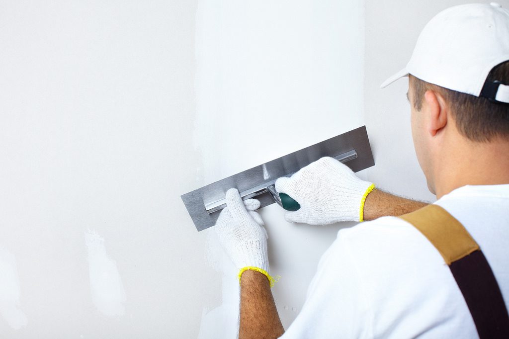 Construction worker wearing gloves and using a tool to apply plaster to a wall. 