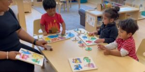 teacher and three preschool-aged children working on puzzles at a child-height table