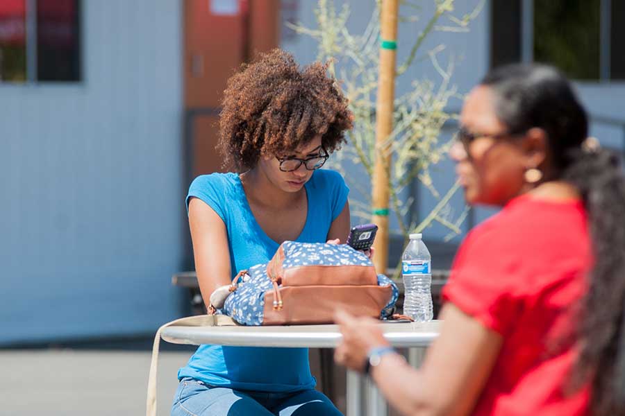 A young woman looking at her phone, seated with her friend.