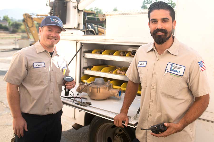 Two smiling water technicians in front of a truck.
